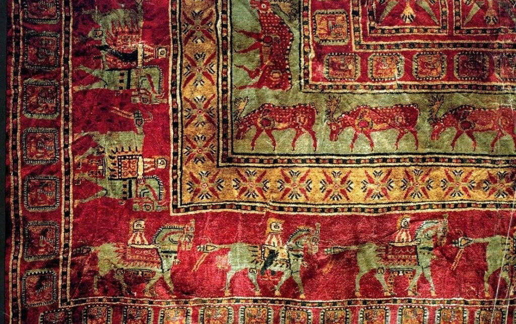 Pazyryk Carpet with vibrant red field, intricate geometric motifs, horsemen border, and deer figures – world’s oldest knotted rug