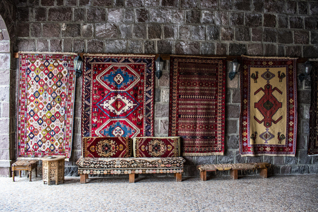 A collection of Anatolian tribal rugs exhibited in a traditional courtyard setting, showcasing bold geometric motifs and regional weaving styles associated with nomadic Yörük culture